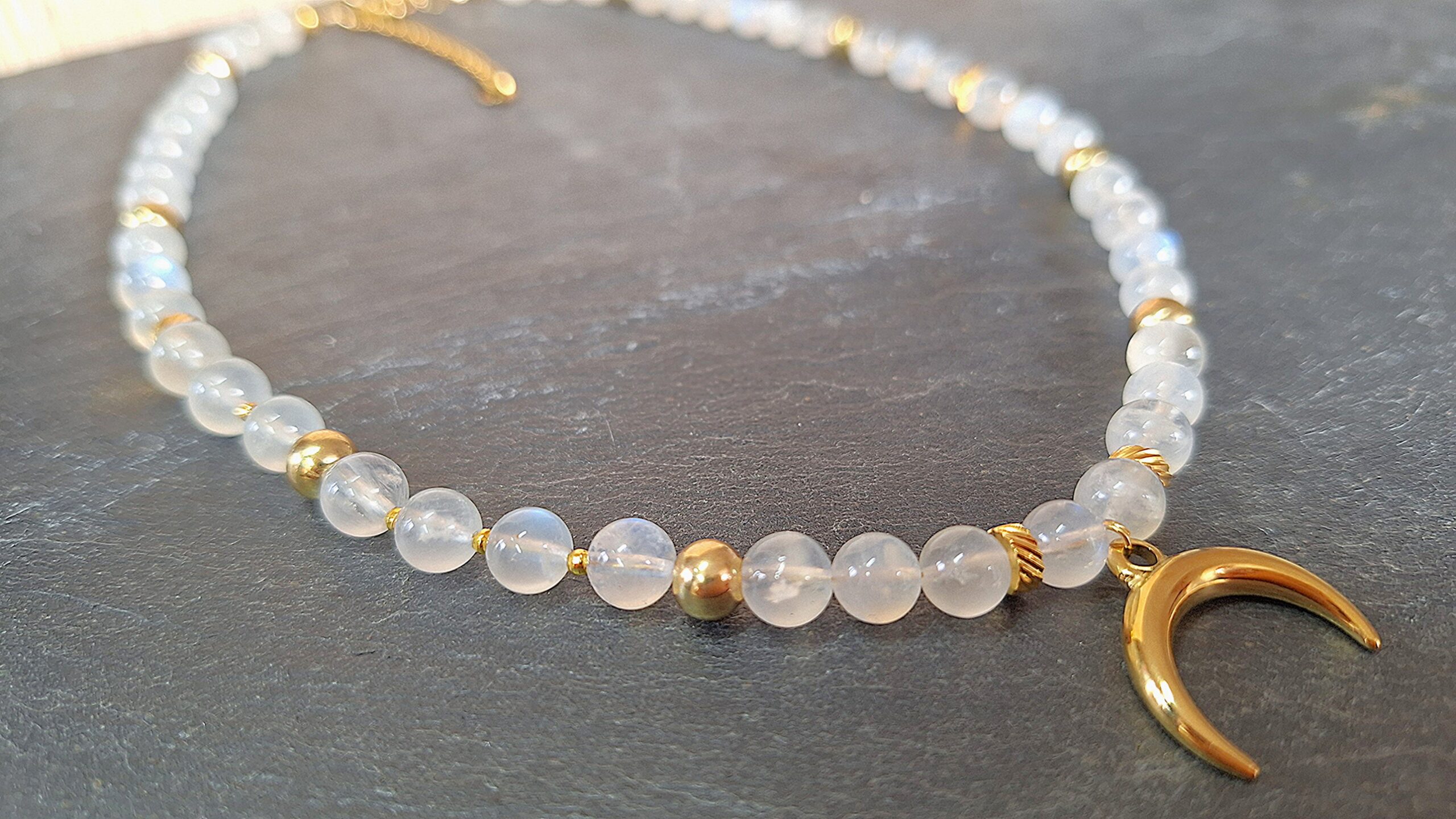 Collier Pierre de Lune & Croissant de Lune doré. Elle est la pierre de la Féminité, de la confiance en soi et de la séduction. Cette pierre dite « d’Aphrodite » fortement YIN : Stimule l’imagination. Apporte poésie, douceur, sensibilité, calme, tolérance, équilibre et confiance en soi. Ouvre à l’inspiration et à l’impulsion. Procure de la profondeur aux sentiments. Contribue au bonheur conjugal. Compense les tendances trop matérialistes, terre à terre. Développe l’intuition et favorise l’ouverture d’esprit. Permet les rêves prémonitoires. Humanise l’acte sexuel (vs procréation). Met en harmonie les cycles hormonaux, aides en cas de troubles menstruels, après un accouchement et lors de la ménopause. Aide à la fertilité.